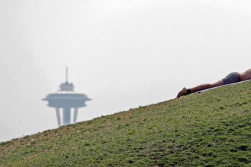A man sunbathes in view of the Space Needle obscured by smoke.