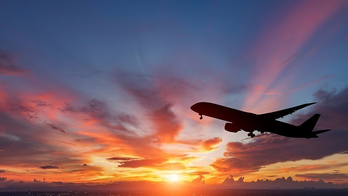 An airplane takes off as the sun sets behind it.
