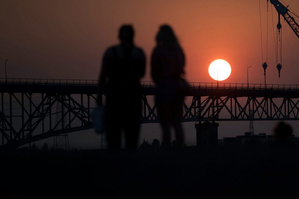 People watching sunset behind bridge