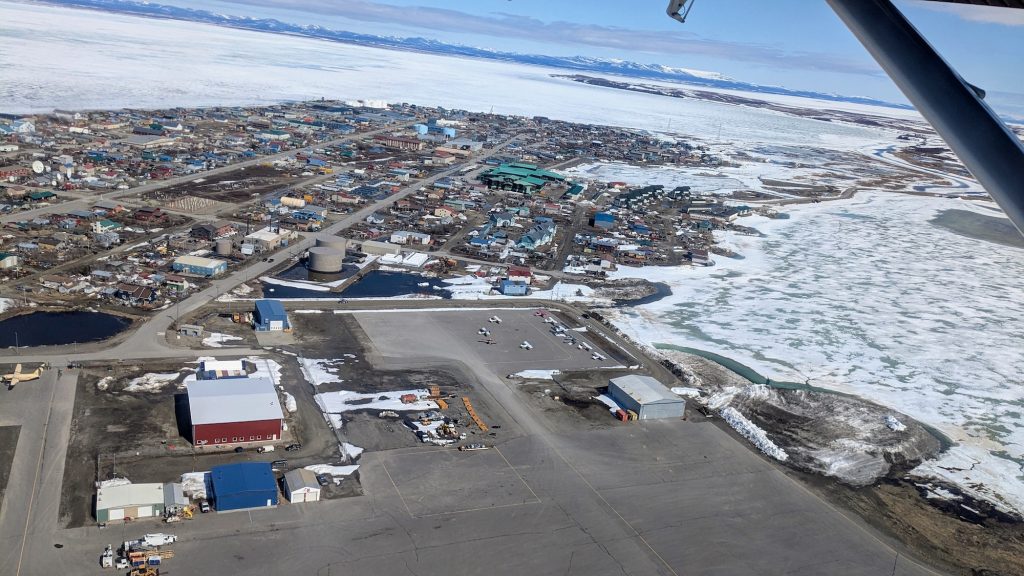 An view of Kotzebue from the sky, showing the small community as well as the frozen over Kobuk Lake and the Chukchi Sea.
