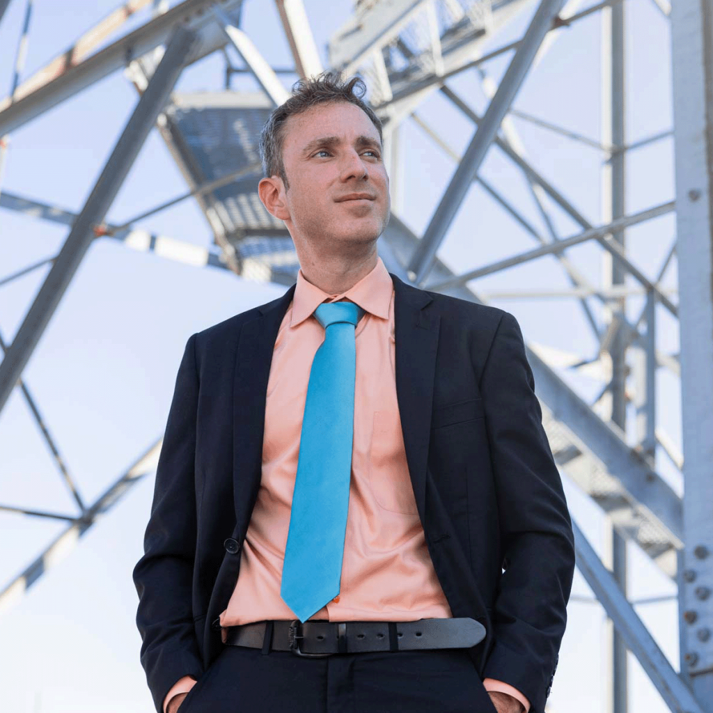 Professor Angel Adames-Corraliza stands in front of a tower, wearing a dark suit with a bright shirt and tie.