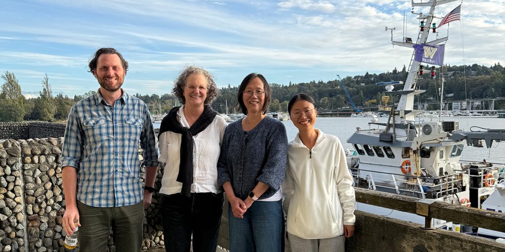 Four researchers pose near the dock, with a University of Washington research vessel in the background.