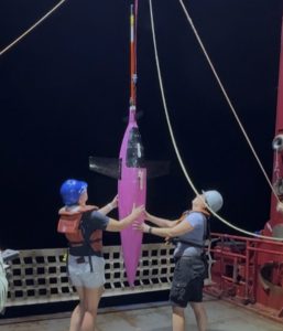 Two researchers guide a Seaglider, which looks like a small, pink torpedo, across the deck of a ship.