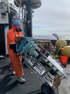 A researcher dressed in an orange jumpsuit rolls equipment across a ship deck. 