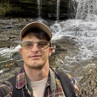 Headshot of Ryan Greenstreet on a hike with a waterfall in the background.