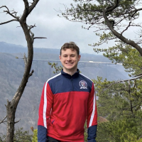 Will Gross on a hike, with trees and a mountain valley in the background.